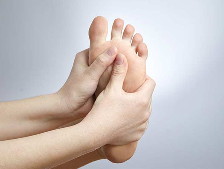 Person holding bottom of their foot because of neuroma foot pain.